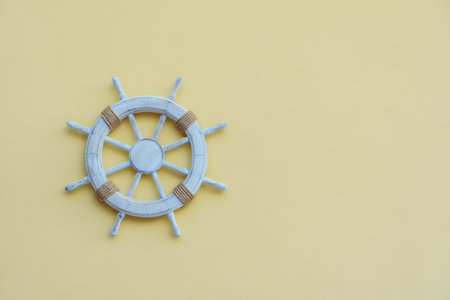 White wooden steering wheel helm decorated with rope hanging on wall on yellow background. Wall decoration, beach, sea travelling, ocean, marine, accessory, navy style, vacation. Isolated, copy space.の写真素材