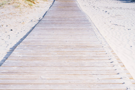 Wooden pathway road boardwalk surrounded by sand with footprints to beach sea ocean on sunny summer day. Summertime, holiday, vacation, travelling, nature, landscape, seashore, coastline, tourism.の写真素材
