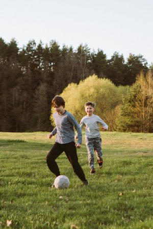 Active boy in light gray longsleeve running behind concentrated teenager who dribbling white ball in...