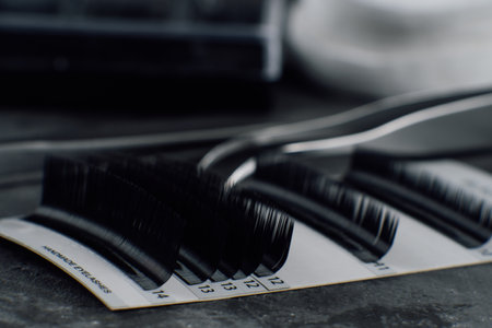 Close-up. Black and white image of a set of various eyelashes for extension and metal tweezers....