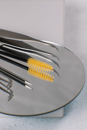 Accessories of cosmetologist and makeup artist tweezers, brush for combing eyebrows and eyelashes, applicators lie on clean mirror surface. Facial care. Space for text. MOCKUP. Beauty industry.の写真素材