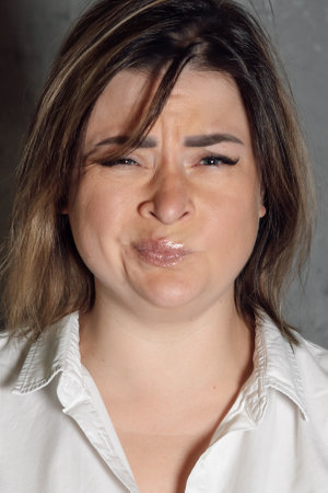 Portrait of funny young woman with brown short haircut squinting sour grimace standing on gray background indoors. Lady with blue eyes in white shirt disgusted, making pouting expression. Vertical.の写真素材