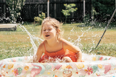 Little girl having fun splashing water in inflatable pool on summer day outside. Games and...