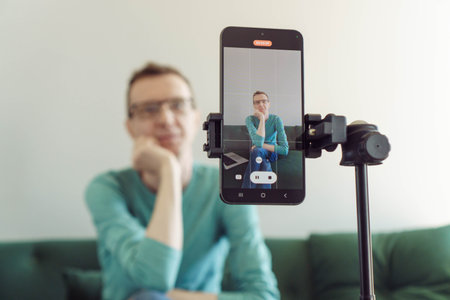 Blogging. In foreground is phone screen mounted on tripod with image from camera of male blogger recording his video. Modern technologies. Online training. Video recording of trainings.の写真素材