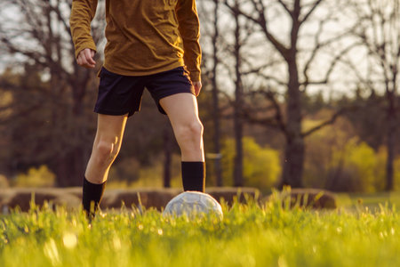 Unrecognizable teenager in sports uniform in early summer morning trains on field against background of forest . Children's sports sections. Hobbies . Football practice. Summer sports camp.の写真素材
