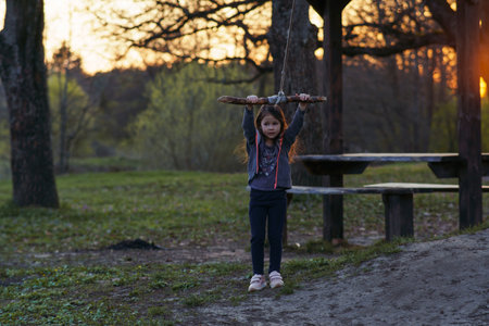 Charming little girl is going to swing on homemade swing in nature, in park, in village, in children's camp. Outdoor games and entertainment. Happy childhood. Summer in country. Child protection.の写真素材