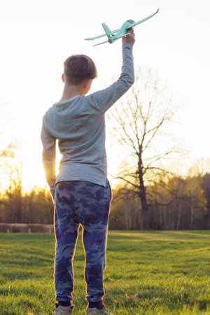 Unrecognizable teenage aircraft modeler stands against sunset with his hand raised up with his airplane. Aircraft modeling classes. Hobbies and hobbies.Happy childhood.の写真素材