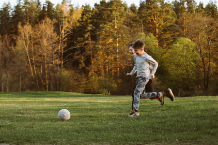 Sports at stadium in park for schoolchildren. Two classmates, brothers in park, in nature on autumn evening playing football. Children's friendship, communication. Happy childhood. Free time.の写真素材