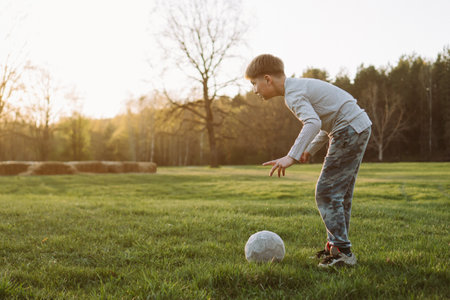Teenager is preparing to hit ball against background of setting sun on autumn evening at stadium. Sports and health. Active games. Physical education lessons. Happy childhood. Free time.の写真素材