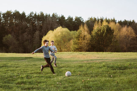 Enjoy playing football. Two teenage friends, brothers in park, in nature on autumn evening. Sports activities. Active games. Health and training. Children's friendship. Happy childhood. Free time.の写真素材