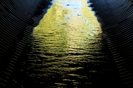 black, corrugated  water-shoot flowing in the green-colored waterの写真素材