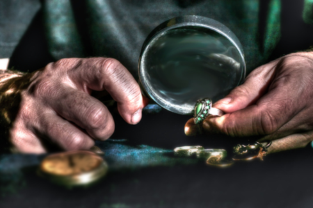 Hands of an old man holding a magnifying glass and magnifying viewer ring