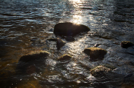 Slightly rough water washed the stones and illuminated by the sun with flaresの写真素材