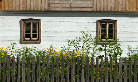 White wall of wooden house with windows, wooden fence and yellow flowersの写真素材