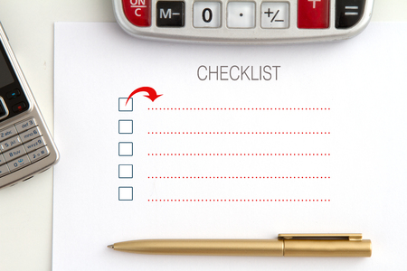 checklist concept - a desk with a list, a calculator, a pen (gold), a mobile phoneの写真素材