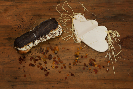 Appetizing, chocolate-coated eclair and two porcelain hearts in a warm, wooden environment