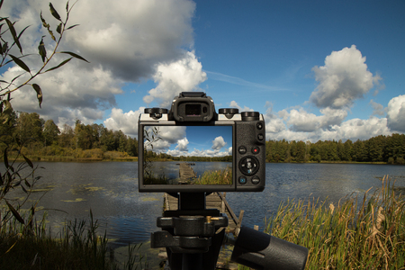 A camera standing on a tripod and taking a picture of a landscape with a lake, landing and cloudsの写真素材