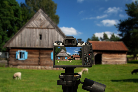 Camera and old wooden house with blue windows and in front of him on the green meadow grazing sheepの写真素材