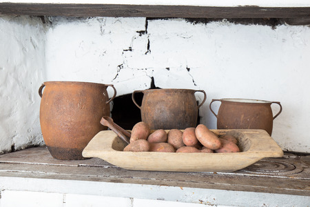 Old cast-iron pots, potatoes in a wooden bowl standing on an old coal kitchenの写真素材