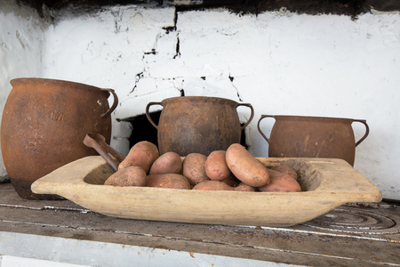 Old cast-iron pots, potatoes in a wooden bowl standing on an old coal kitchenの写真素材