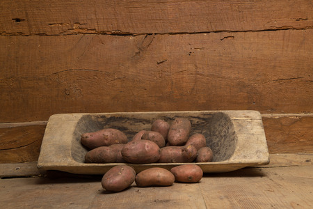 Purple potatoes in a wooden bowl standing on a wooden floor against the background of a wooden wallの写真素材