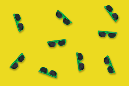 Green sunglasses lying on a yellow like seaside sand backgroundの写真素材