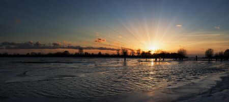 Sun rays shining through the trees on the ice-covered river.の写真素材