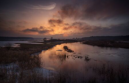 Great view of the red sun setting over the spilled winter riverの写真素材