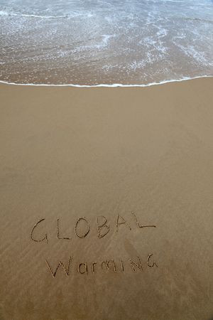 Global warming written in the sand at beach with rising waveの写真素材