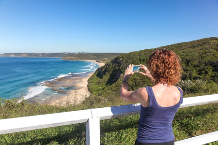 A women takes a photo with her smart phone of Burwood Beach - Newcastle Australia. The Newcastle region is home to some amazing coastline.の写真素材