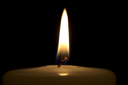 A burning candle isolated on a black background with the focus on the burning candle-wick.の写真素材