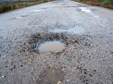 Pothole on a paved road on a rainy winter day. Concept of risk and traffic problemsの写真素材
