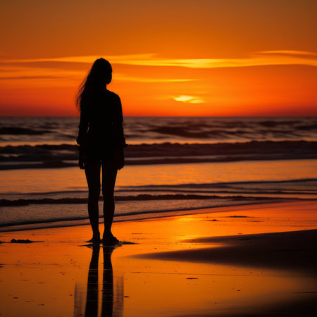 Silhouette of a woman standing on the beach at sunset.の素材