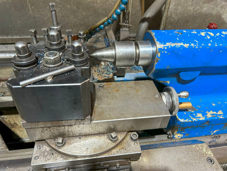 Close-up of a metal lathe machine with steel components in a workshop, featuring bolts, gears, and a blue-painted part.の写真素材