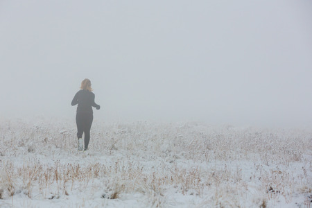 A female trail runs in the fog and snow of winter.の写真素材