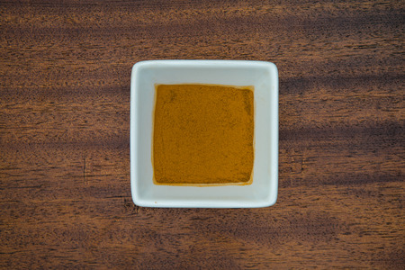 Cinnamon sits in a square white bowl on a real wood background.の写真素材