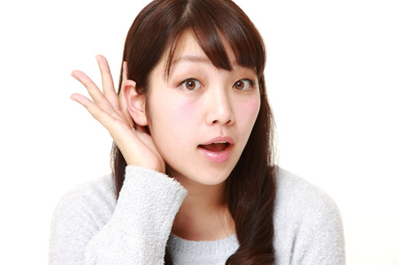 young woman with hand behind ear listening closelyの写真素材