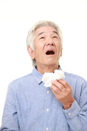 senior Japanese man with an allergy sneezing into tissueの写真素材