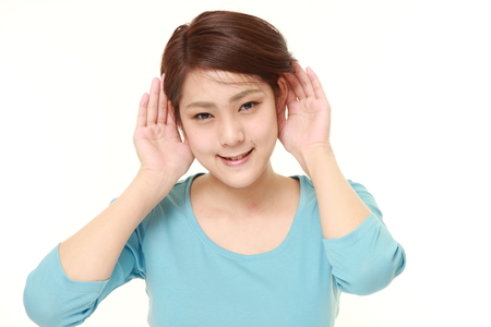 young woman with hand behind ear listening closelyの写真素材