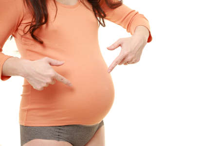 pregnant woman pointing to her stomach in studio shot on white backgroundの写真素材