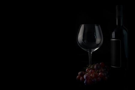 Wine bottle, grapes and a wine glas against a dark background. With copyspace for your own text.の写真素材