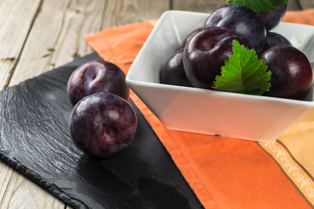 Autumn harvest. Fresh plums in a bowl. Stone plate and a wooden background.の写真素材
