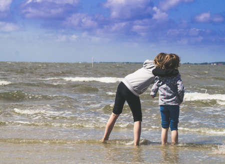 Bensersiel, Germany - Juni 26, 2017: Two girls are on the beach with thier feet in water. A sunny but windy day at the german north sea coast.のeditorial素材