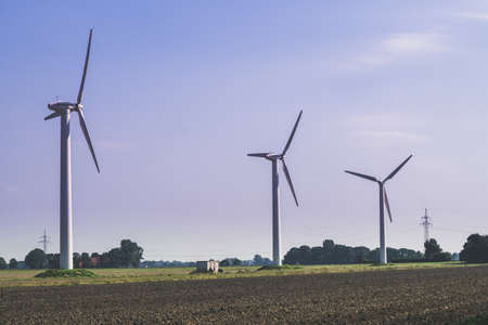 Wittmund, Germany - September 10, 2016: Group of three wind turbines mills against the sky and a field of black soil. Clean energy concept.のeditorial素材