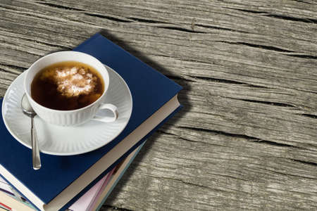 Cup of tea with milk on a stack of books. Wooden table background.の写真素材