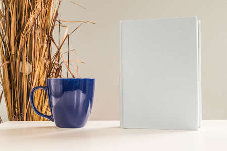 White blank closed book and blue coffee cup on a table.の写真素材