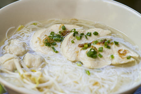 Thai noodle soup with fish ball in white ceramic bowl on brown wooden table - close up top view