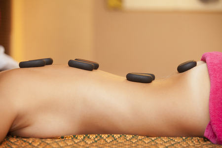 Beautiful woman having hot stones on her back in spa salon. concept of healthcare and female beauty. view of the woman's back with hot stones from the frontの写真素材