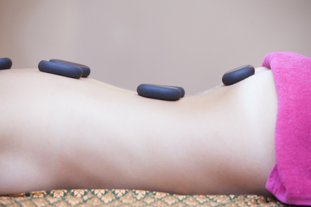 Beautiful woman having hot stones on her back in spa salon. concept of healthcare and female beauty. view of the woman's back with hot stones from the frontの写真素材