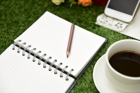 Have a cup of black coffee.Writing on copy space note book . with Pencil on green grass Background.With selective focus.の写真素材
